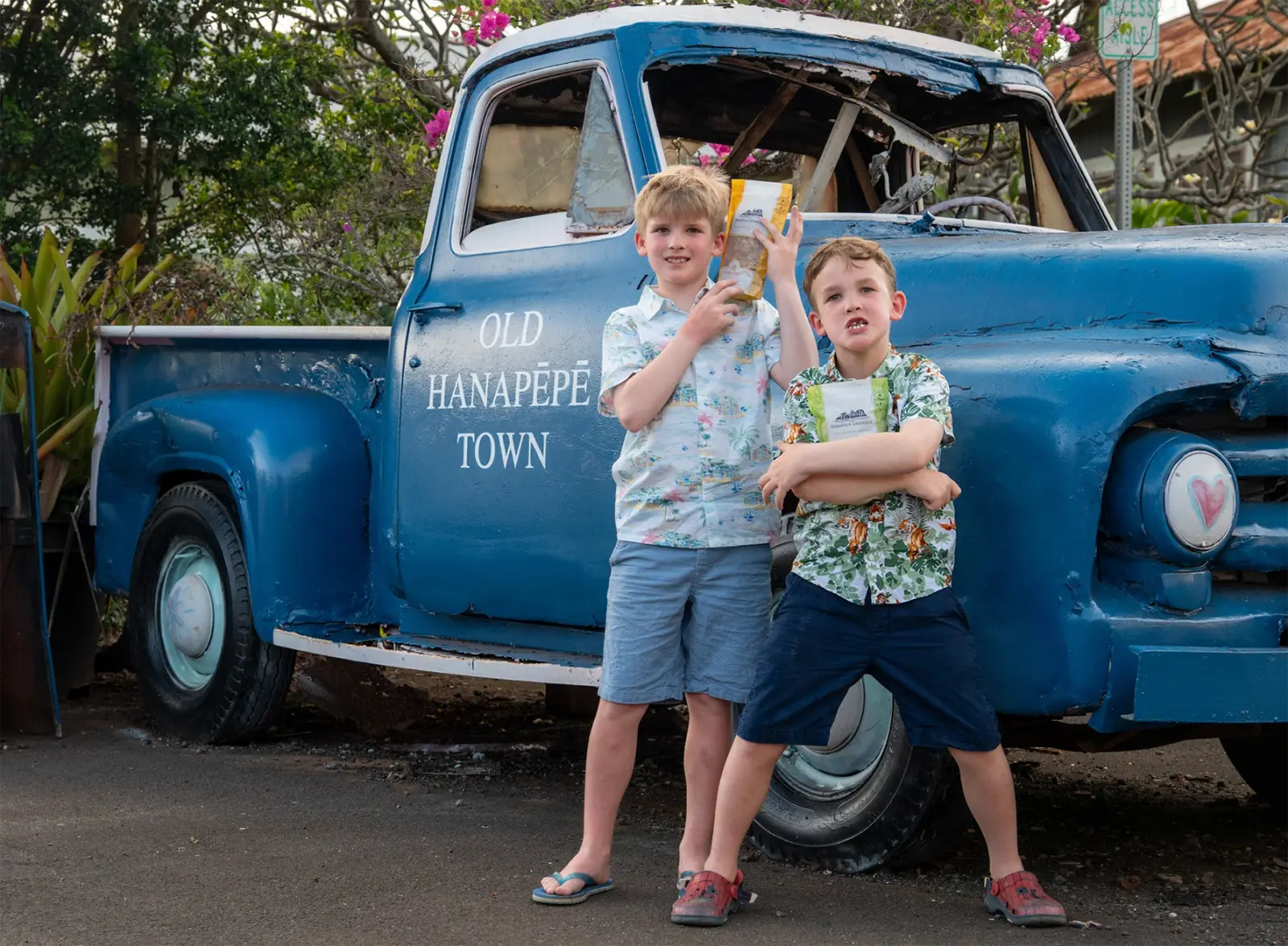 Two children standing in front of an old blue truck with 'Old Hanapepe Town' written on it.