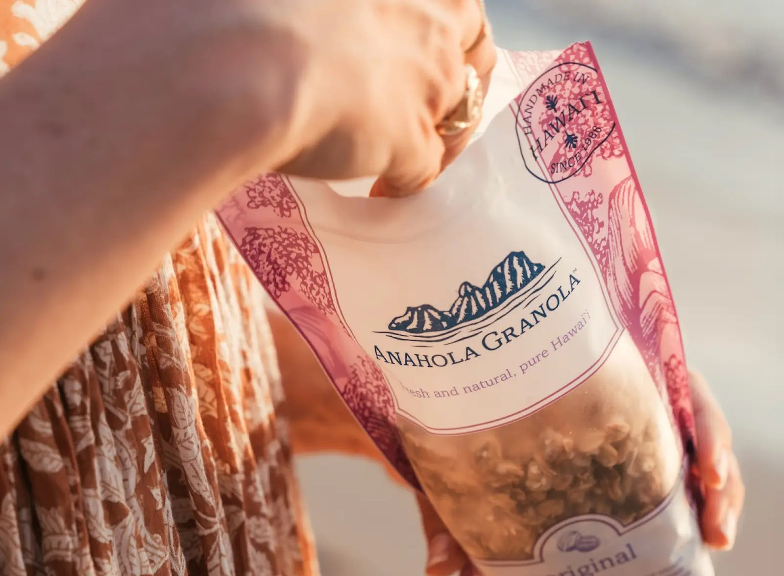 Close up of a person holding a bag of original Anahola Granola with a blurred background