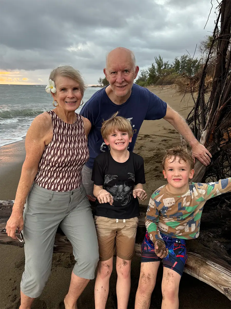 Becky, Stewart, and their two grandsons on a beach in Hawaii.