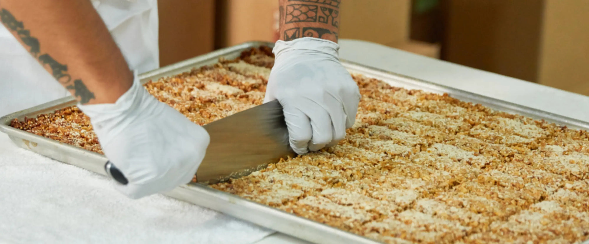 Person wearing gloves slicing granola on a baking sheet.